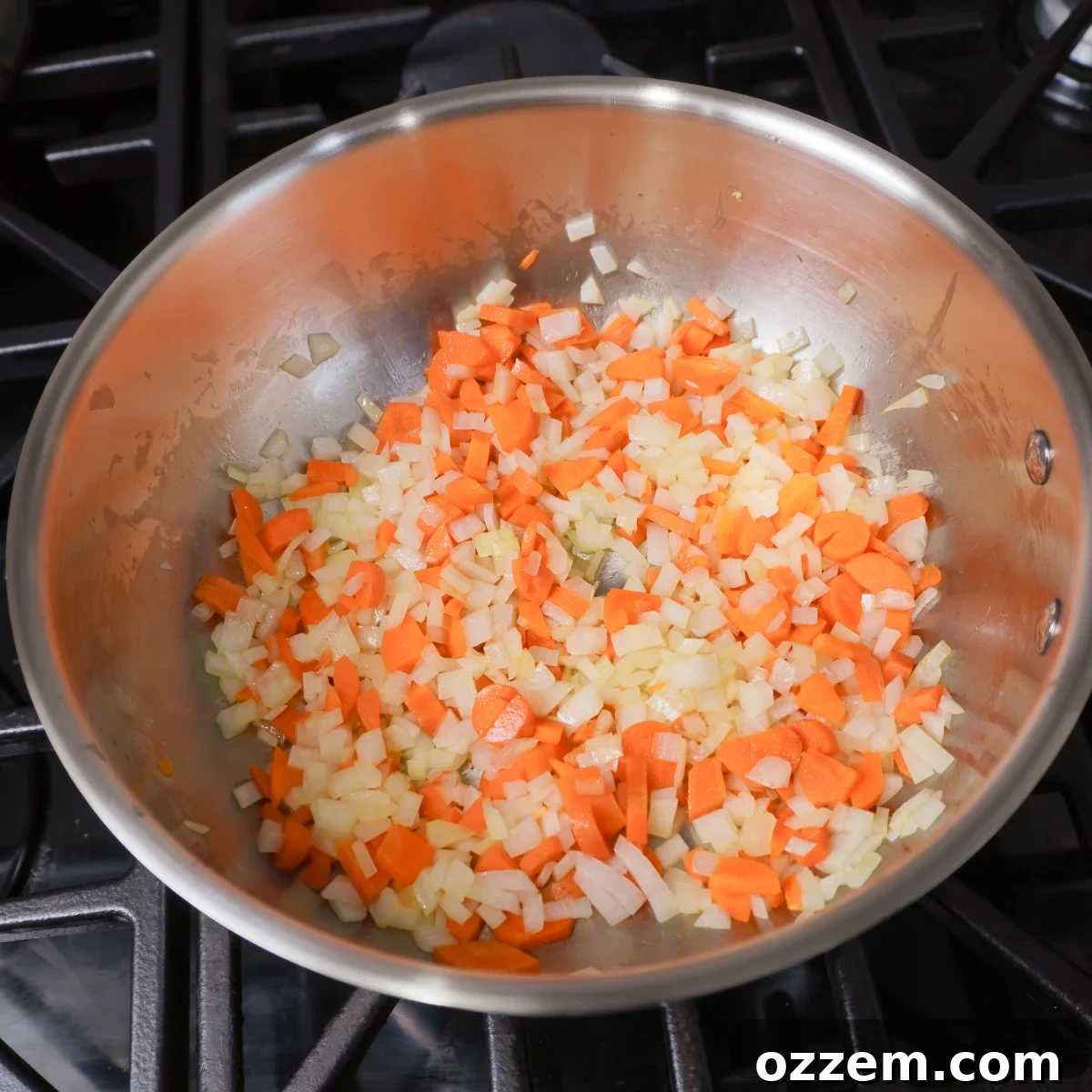 Sautéed onion, carrots, and garlic simmering in a metal saucepan on the stovetop, forming the aromatic base for the pie filling.