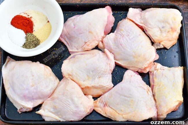 raw chicken thighs and seasoning in a bowl on a metal sheet tray