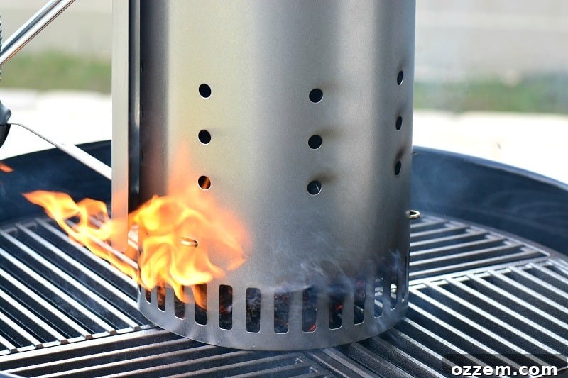 Close-up of a long-reach lighter igniting newspaper in the bottom of a chimney starter