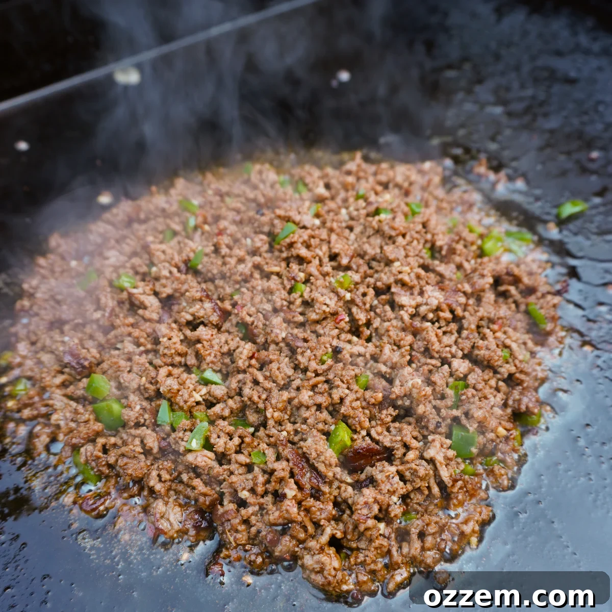 Sizzling ground beef mixed with melted American cheese and sautéed onions and peppers on a griddle.