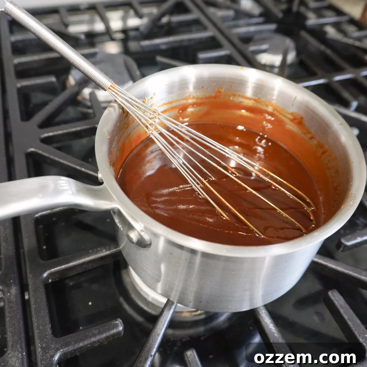 BBQ sauce simmering in a saucepan on the stove, with a whisk stirring the mixture.
