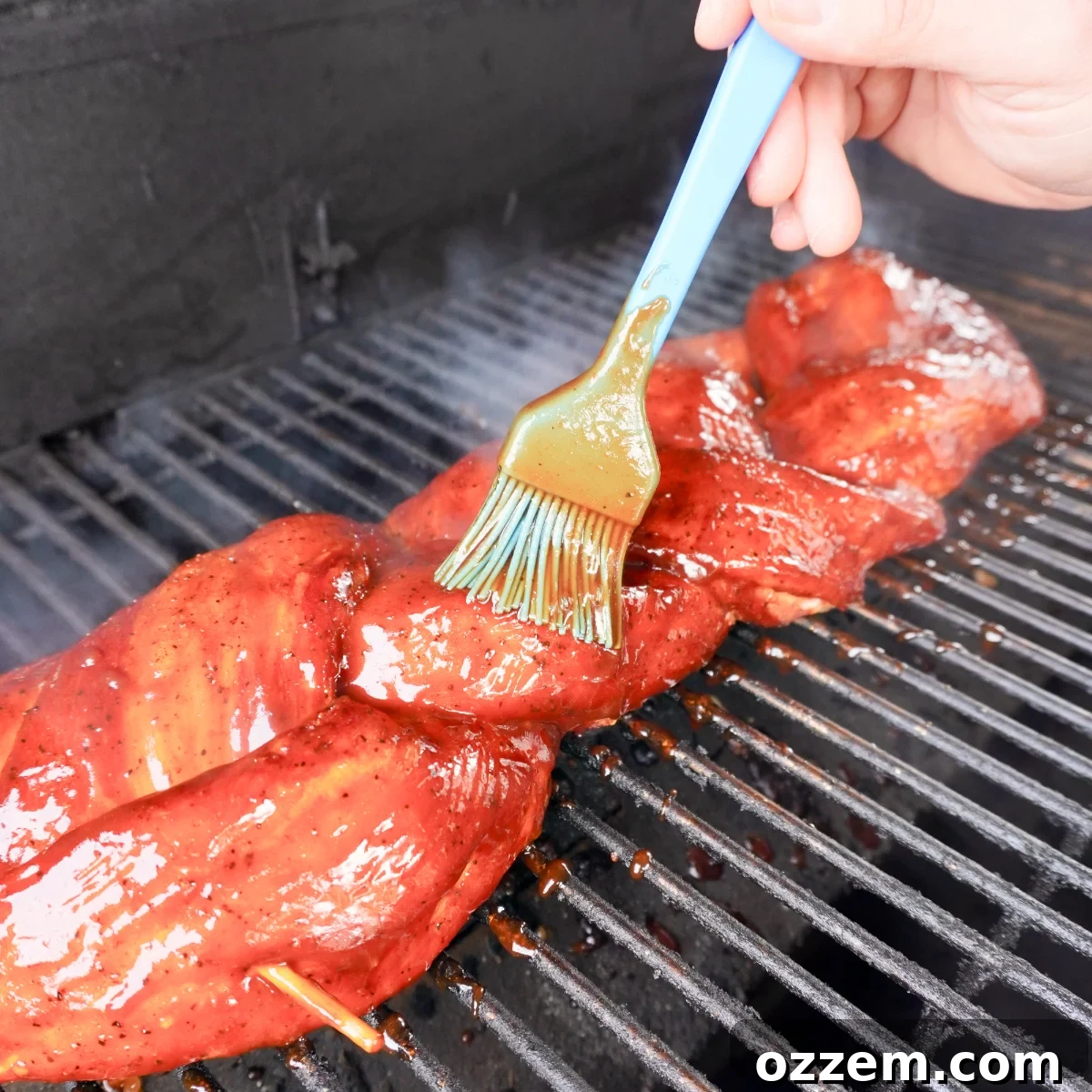 Grilled pork being brushed with sweet and tangy BBQ sauce on the grill.