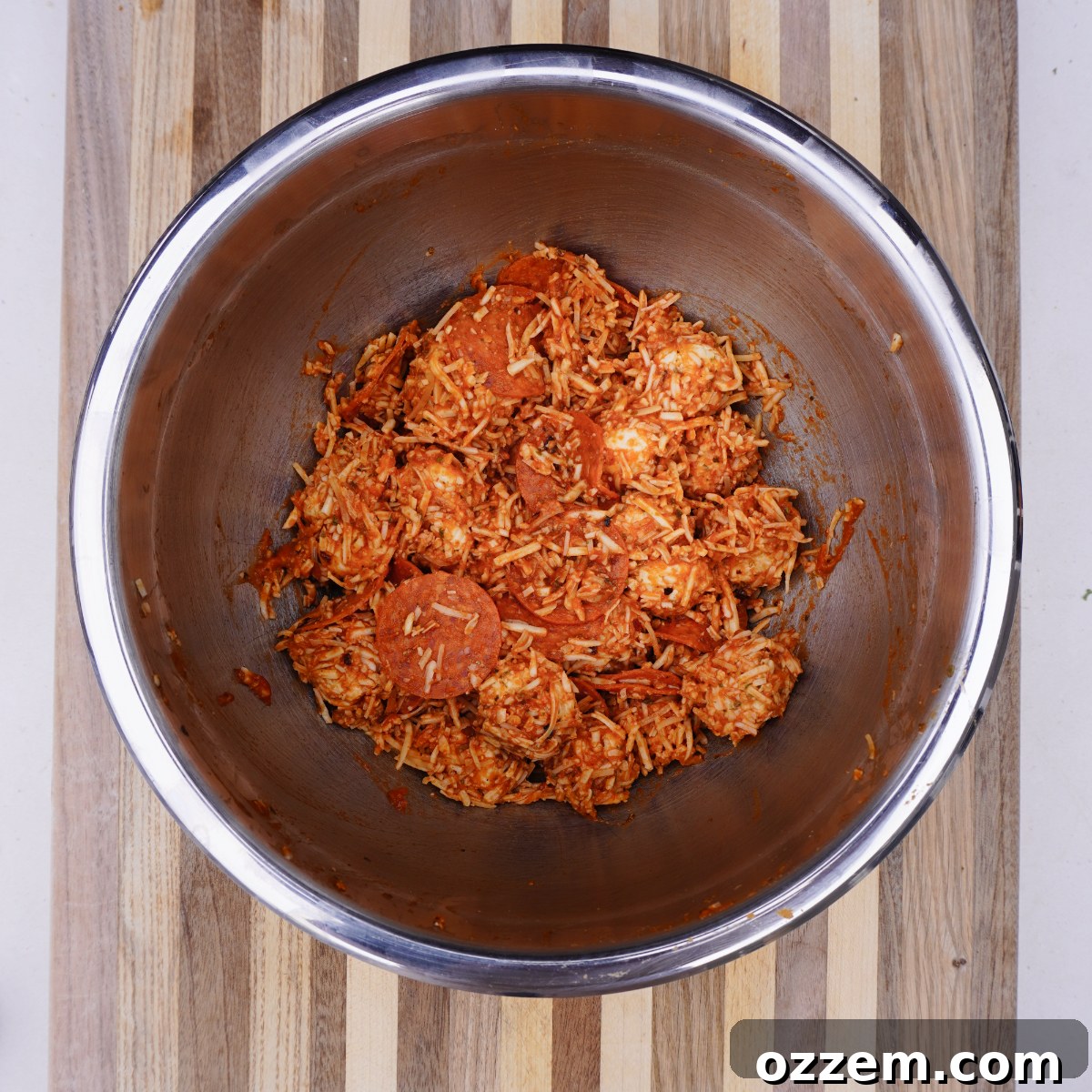 All pizza ingredients mixed together in a large bowl, ready for baking or grilling, showcasing the saucy and cheesy biscuit pieces