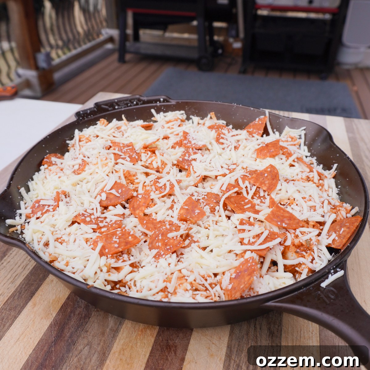 Prepped pull apart pepperoni pizza mixture in a cast iron skillet, topped with extra cheese and pepperoni, ready for the grill