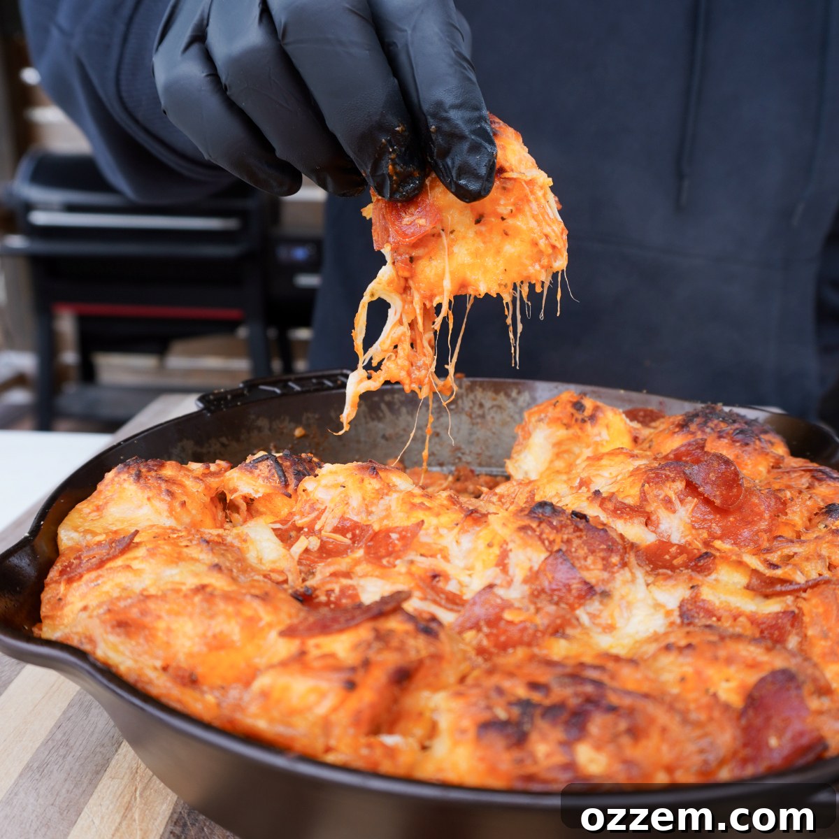 A single cheesy and saucy biscuit piece being pulled from the hot cast iron skillet, showcasing the melted cheese stretch