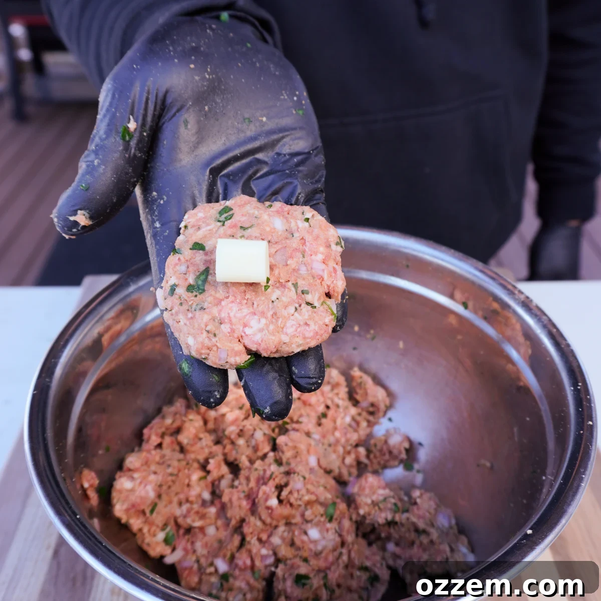 A piece of mozzarella cheese placed in the middle of a flattened meatball mix patty.