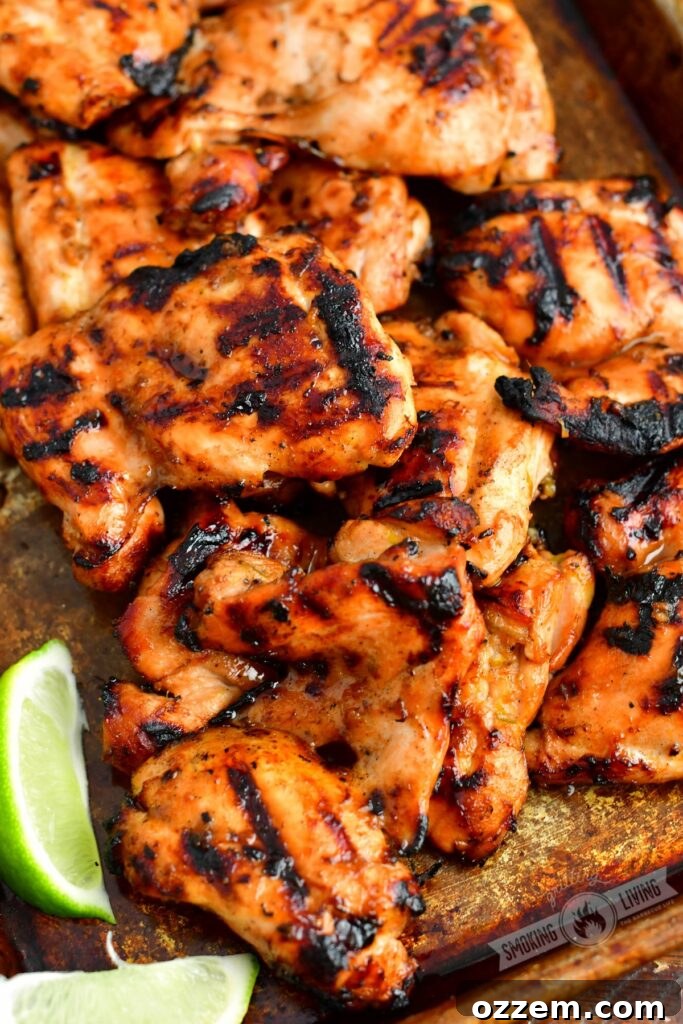 Zesty Grilled Ginger Lime Chicken Thighs 2 Perfectly grilled chicken thighs arranged on a metal sheet pan, garnished with fresh lime wedges