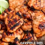 closeup of grilled chicken thighs and lime wedges on a metal pan