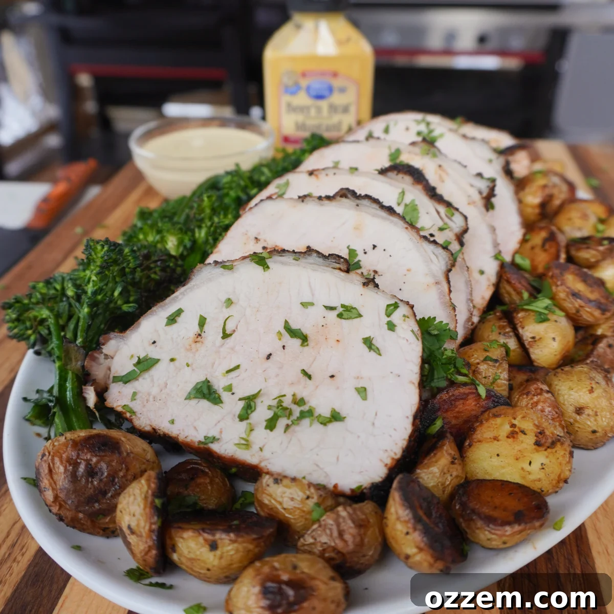 Grilled mustard pork loin sliced on a plate with roasted potatoes and broccolini.