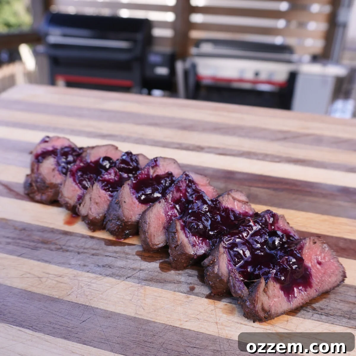 Perfectly grilled venison tenderloin sliced on a cutting board topped with homemade blueberry sauce, ready to serve.
