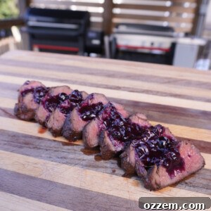 Perfectly grilled venison tenderloin sliced on a cutting board topped with blueberry sauce.