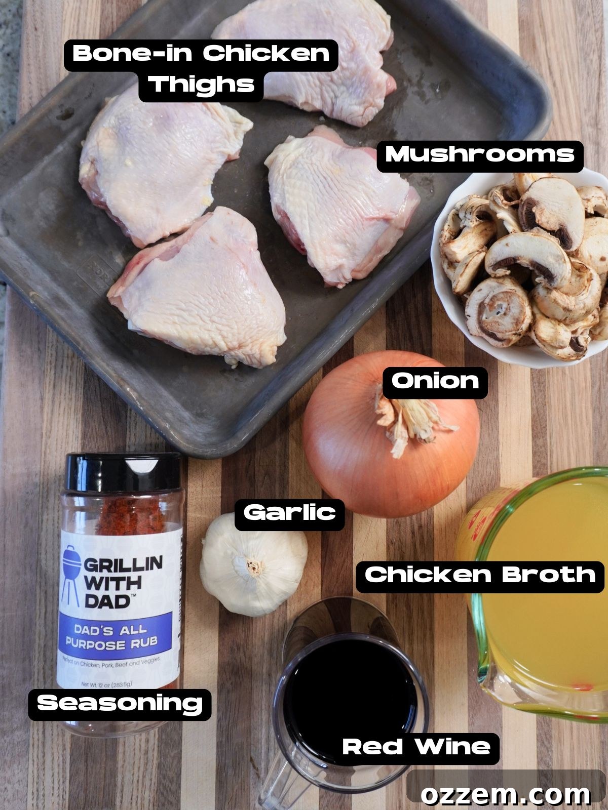 Fresh ingredients laid out for braised chicken, including chicken thighs, mushrooms, onions, garlic, tomatoes, and herbs.