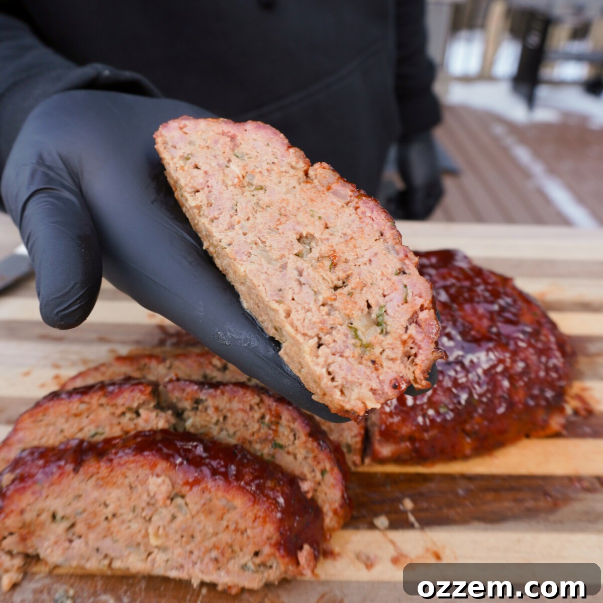 A slice of moist smoked meatloaf held by hand, showing its tender texture.