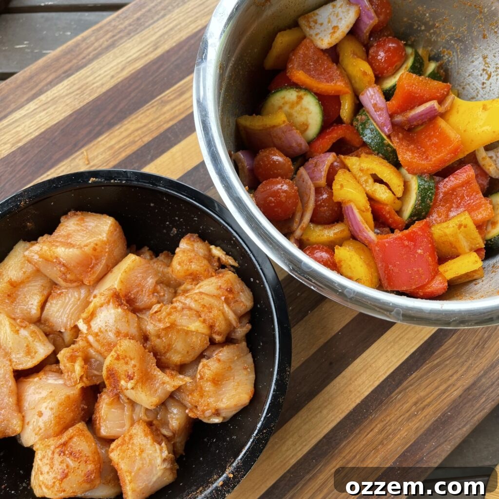 Close-up of cubed chicken and chopped vegetables like bell peppers, zucchini, and grape tomatoes, ready for skewering.