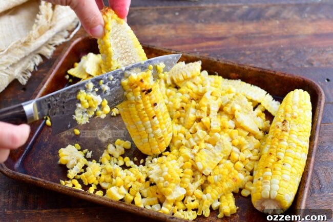 person cutting corn kernels off of grilled corn on the cob into a large bowl