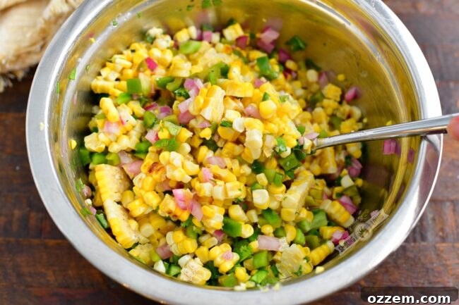 mixing ingredients for the corn salad in a metal bowl with a spoon