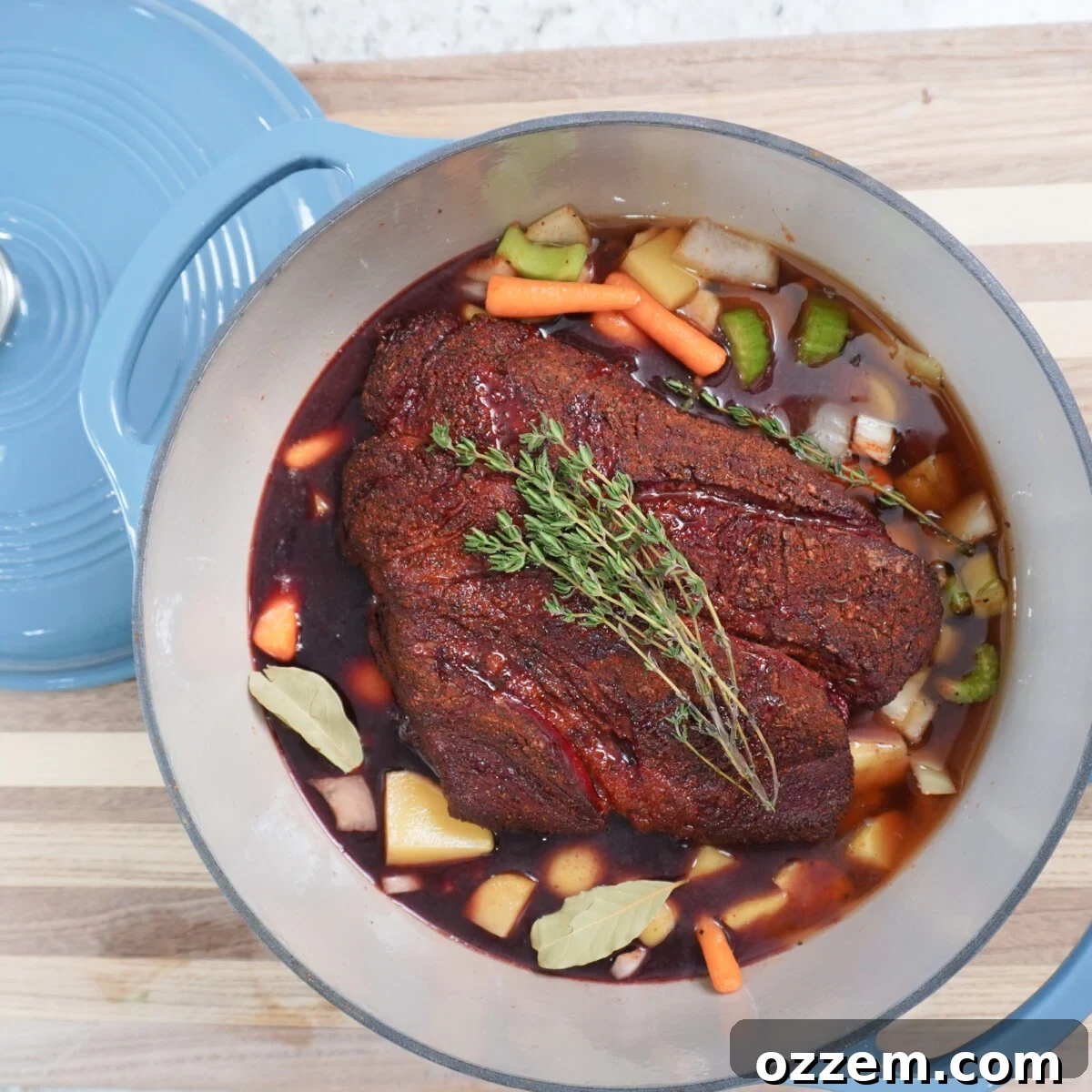 A smoked chuck roast nestled on a bed of vegetables in a Dutch oven with braising liquid, ready for braising.