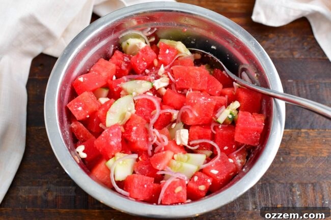 Summer Watermelon Feta Delight 7 A wooden spoon gently tossing watermelon, cucumber, shallots, and feta cheese in a mixing bowl.