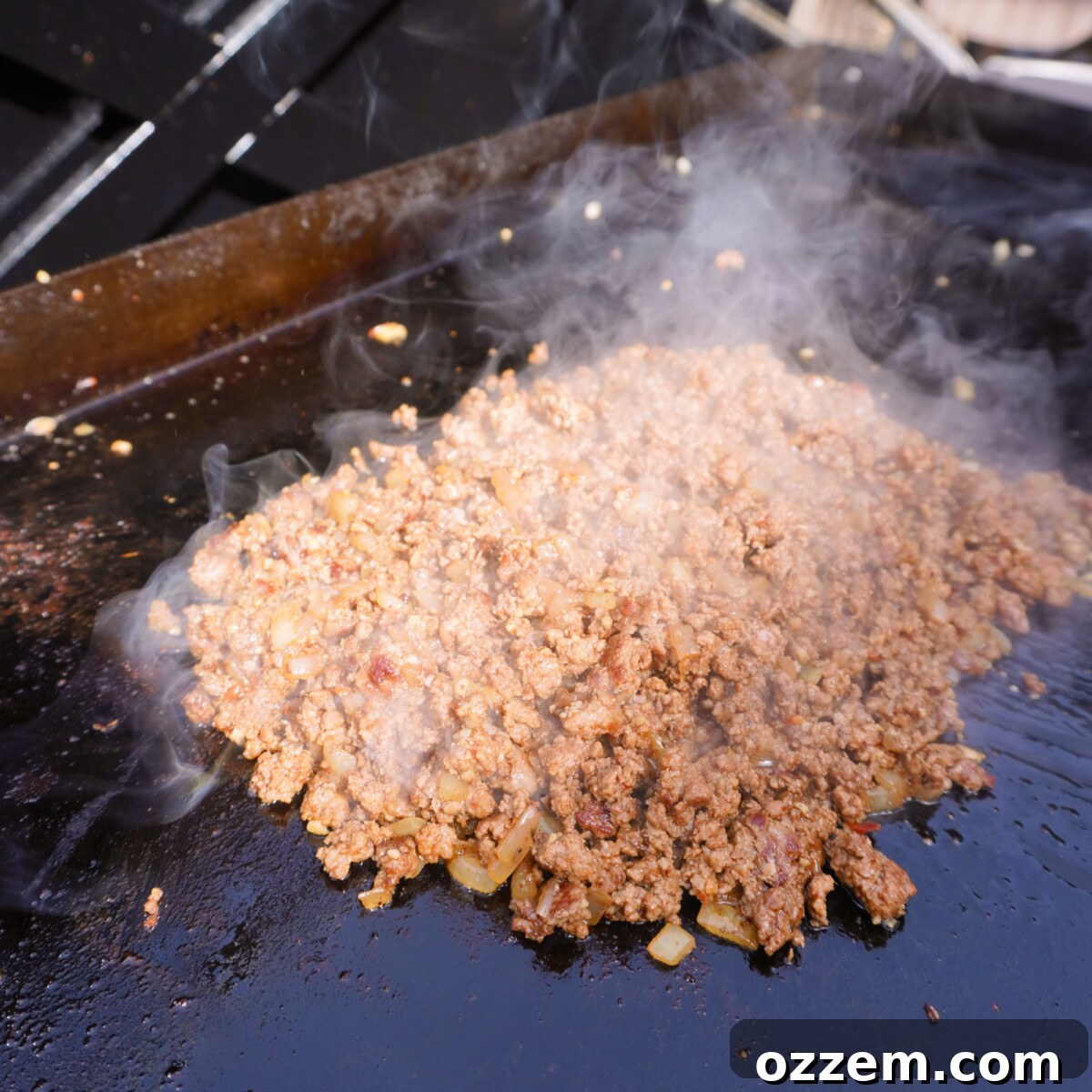 Sizzling ground beef and sautéed onions perfectly mixed together on a griddle, seasoned and browned.