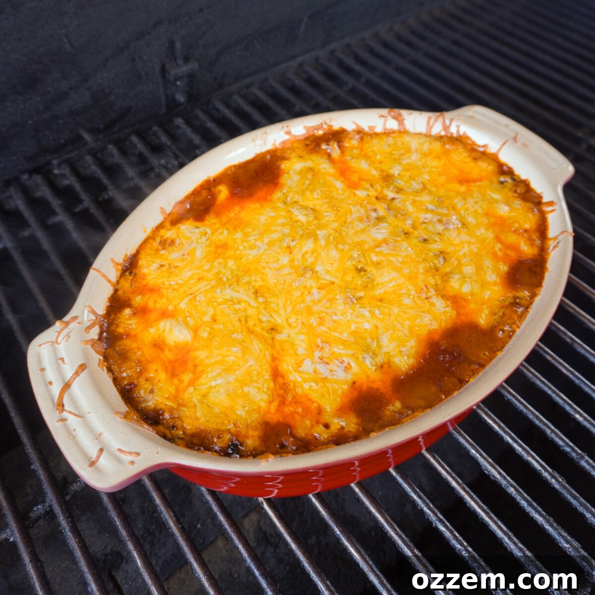 A bubbling Smoked Beef Enchilada Casserole cooking inside a grill, with cheese melting perfectly over the top.