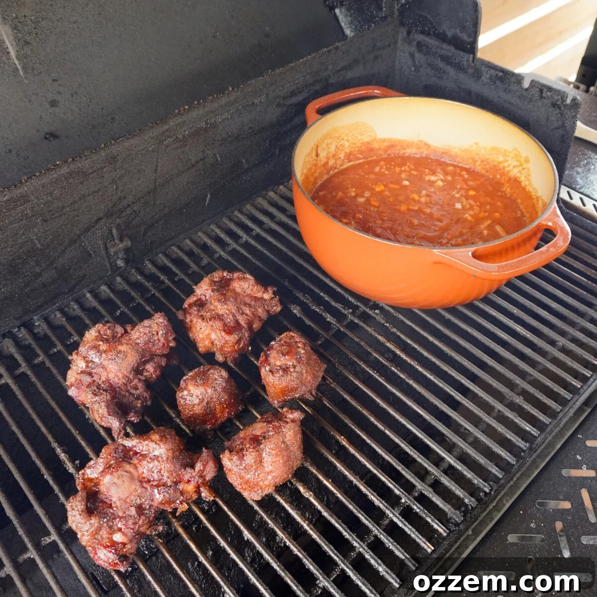 Seasoned oxtail and braising liquid in a Dutch oven on a grill.
