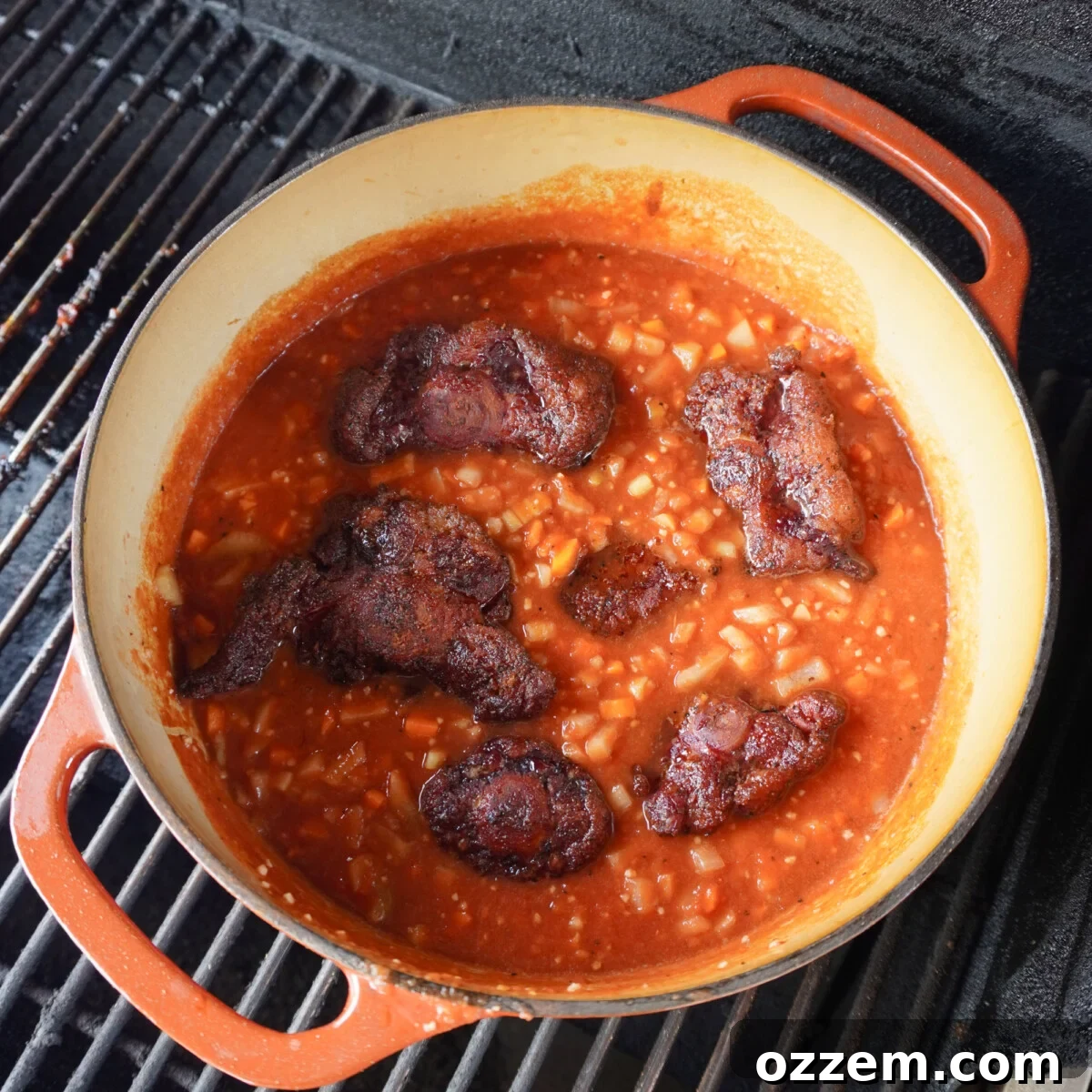 Dutch oven with braising oxtail placed on a smoker grill.