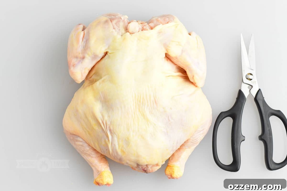 whole chicken on white cutting board with kitchen scissors next to it, preparing for backbone removal