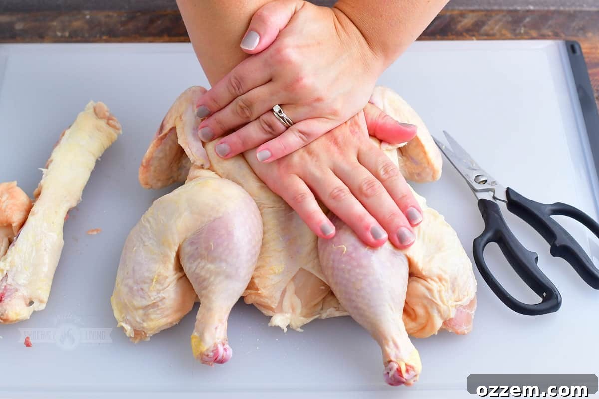 pushing on the breastplate of the butterflied chicken to ensure it lays flat