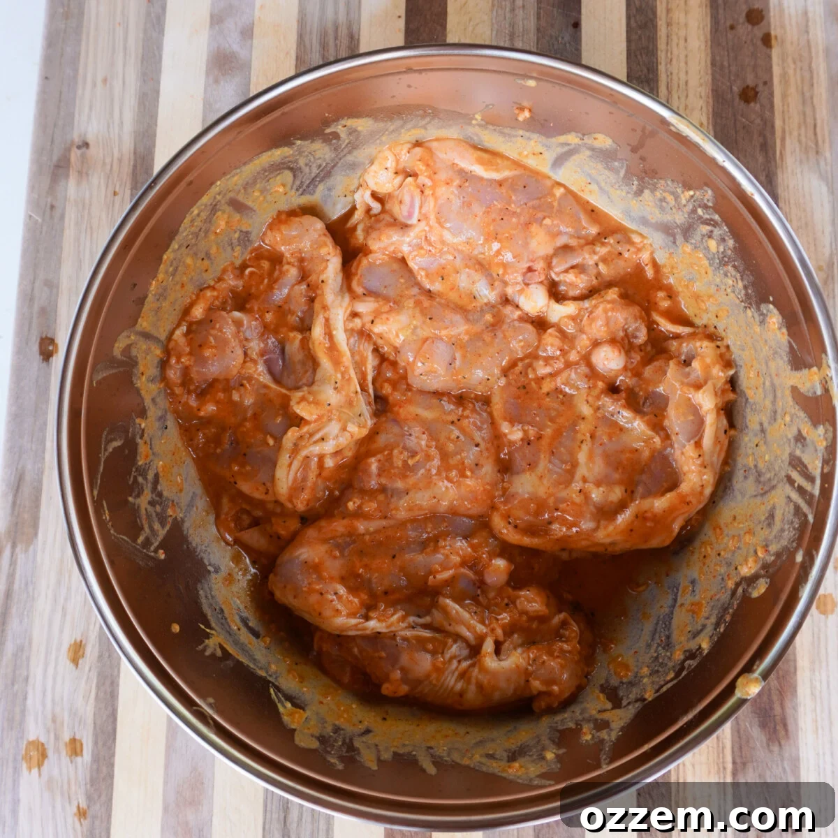 Raw chicken thighs marinating in a zesty lemon dill sauce in a bowl, ready for grilling.