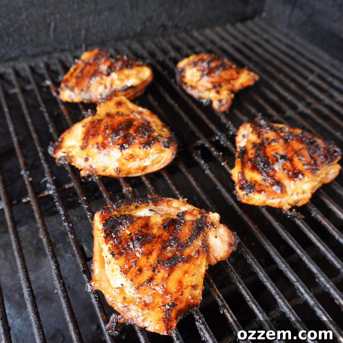 Crispy grilled chicken thighs resting on a grill grate, showcasing perfect sear marks and golden skin.