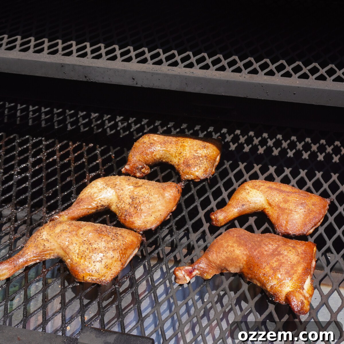 Sweet tea brined smoked chicken quarters on a smoker grate, with smoke wafting.