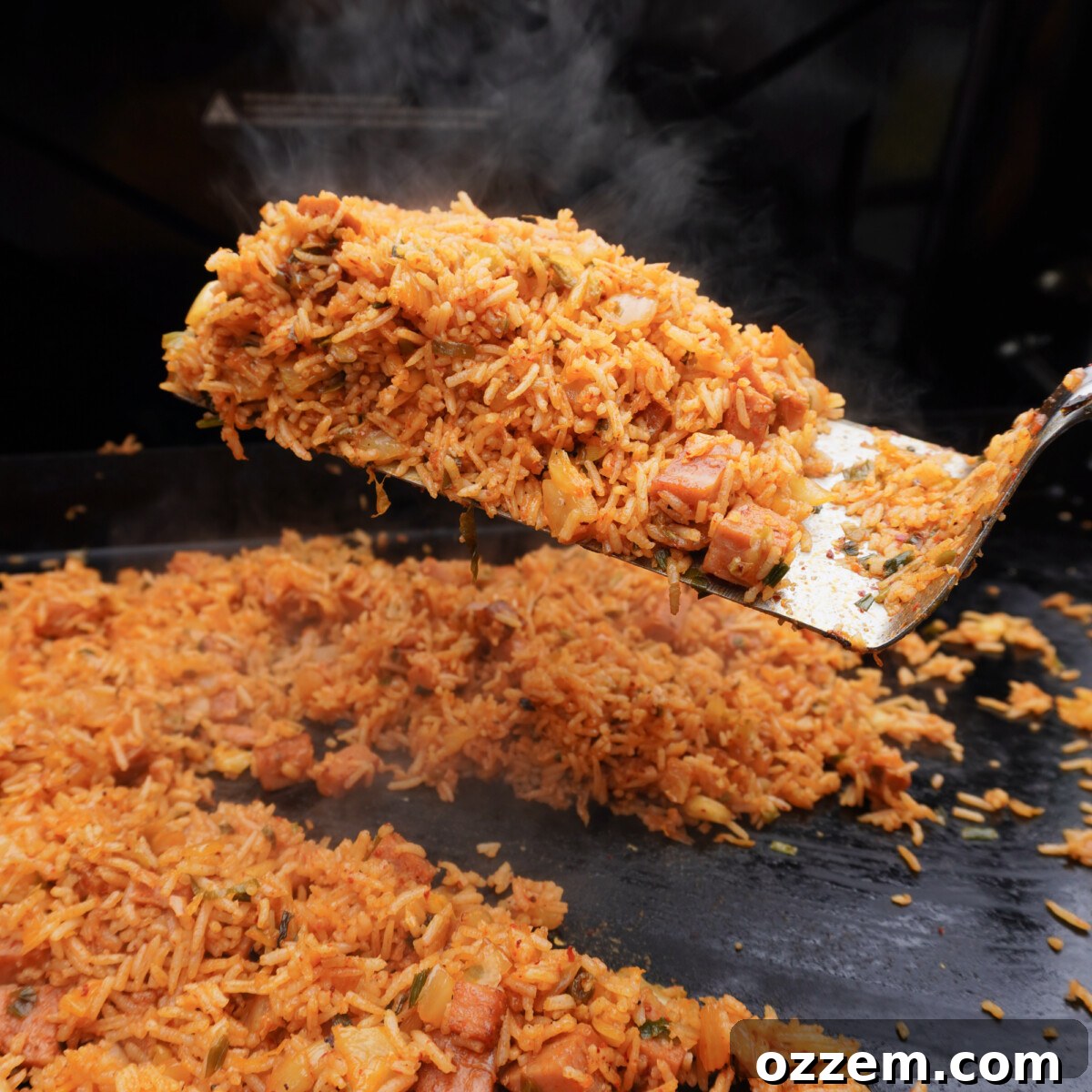 Close-up of Kimchi Fried Rice being cooked and mixed on a griddle, showing the vibrant colors and textures.