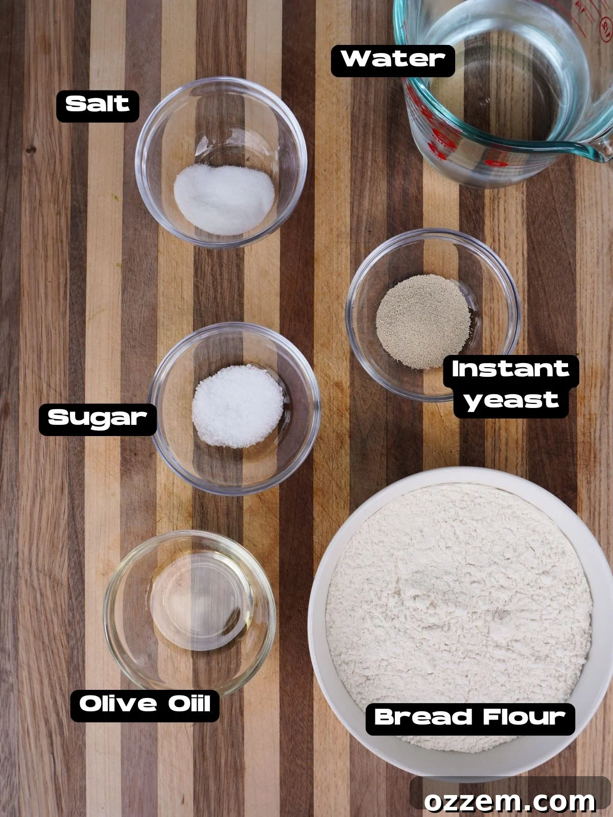 A selection of fresh ingredients laid out for making pizza dough, including flour, water, yeast, sugar, salt, and olive oil.