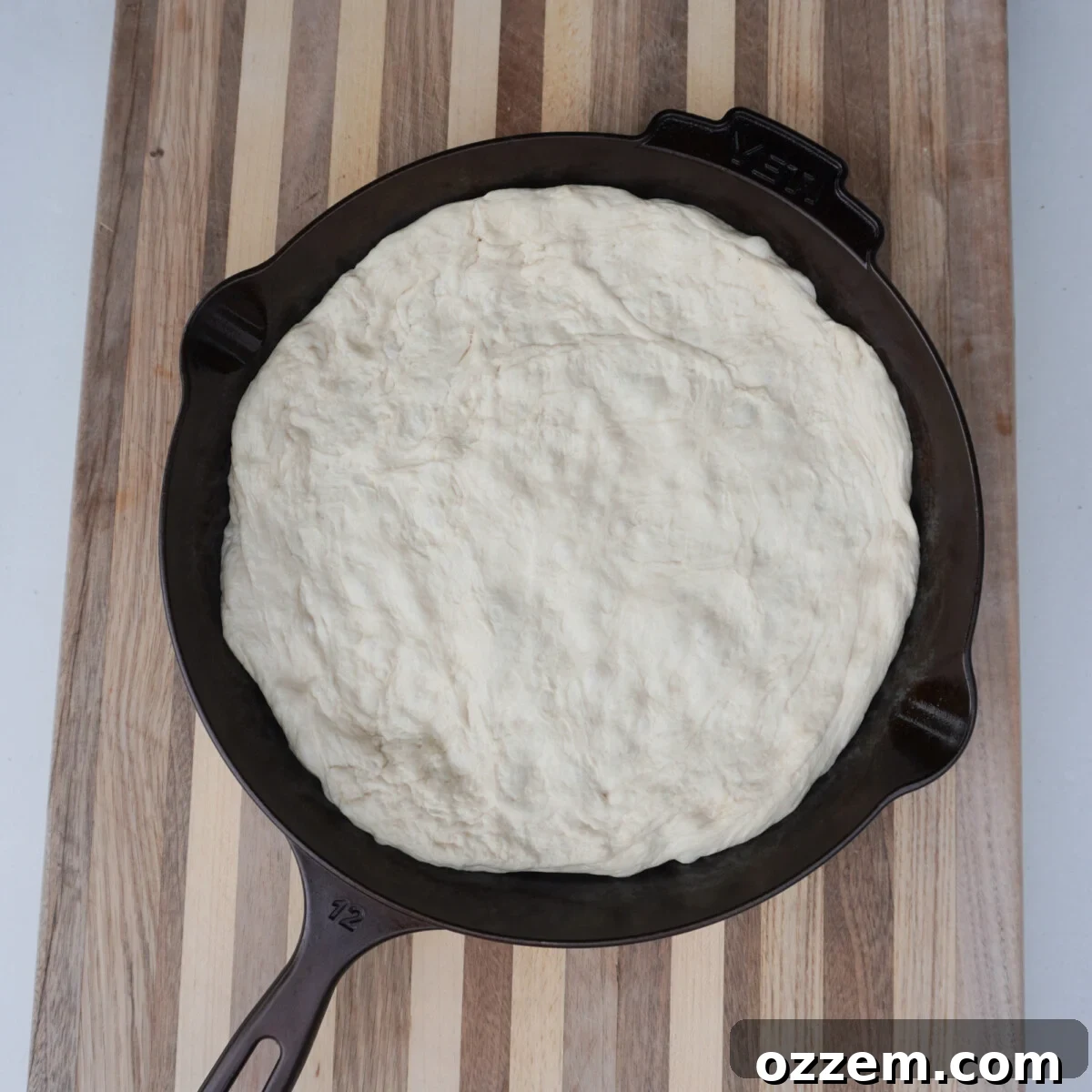 Raw pizza dough pressed into a well-oiled Yeti cast iron skillet, ready for its second proof.