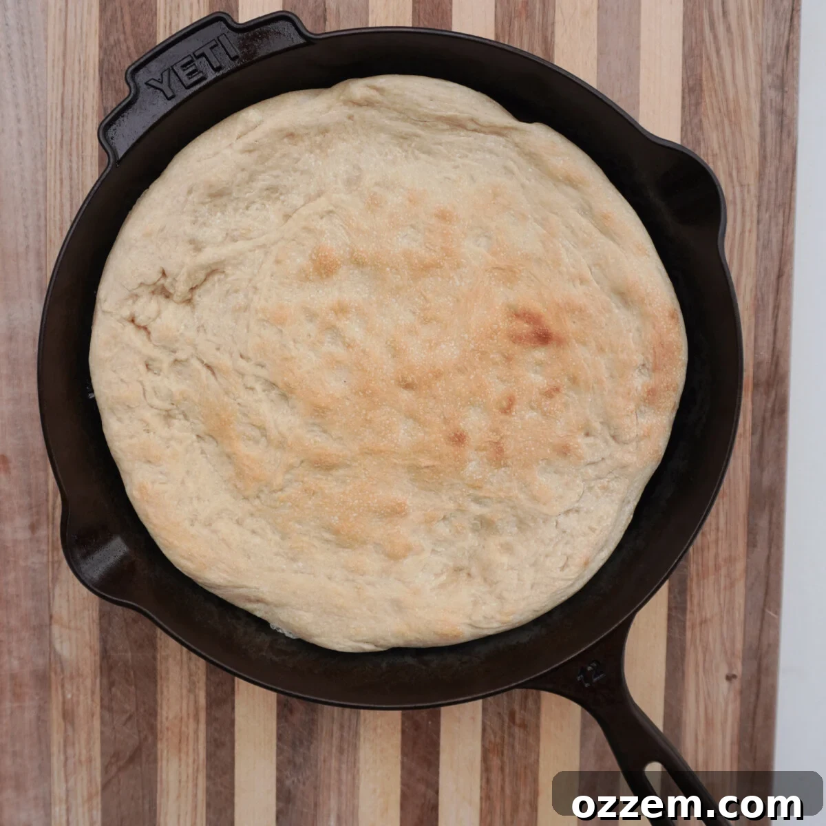 Pre-baked pizza dough in a Yeti cast iron skillet on a wooden cutting board, ready for toppings.