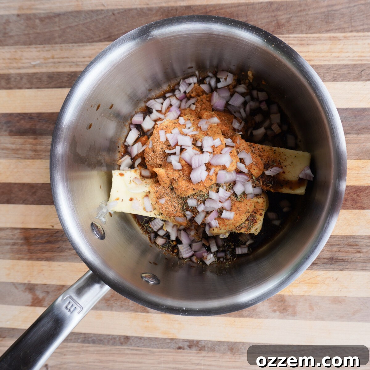 Ingredients for cowboy butter sauce simmering in a saucepan on a grill, highlighting the rich colors and textures of the melting butter, garlic, and spices.