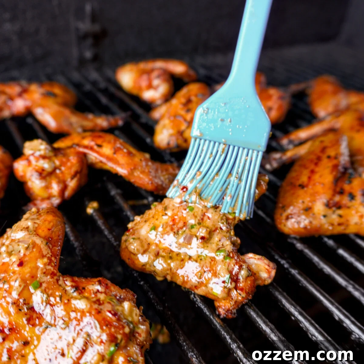 Cowboy butter sauce being brushed onto grilled chicken wings still on the grill grates, creating a glistening, flavorful coating.