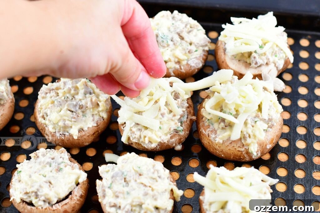 A hand sprinkling shredded Mozzarella cheese over stuffed mushrooms on a tray before smoking.