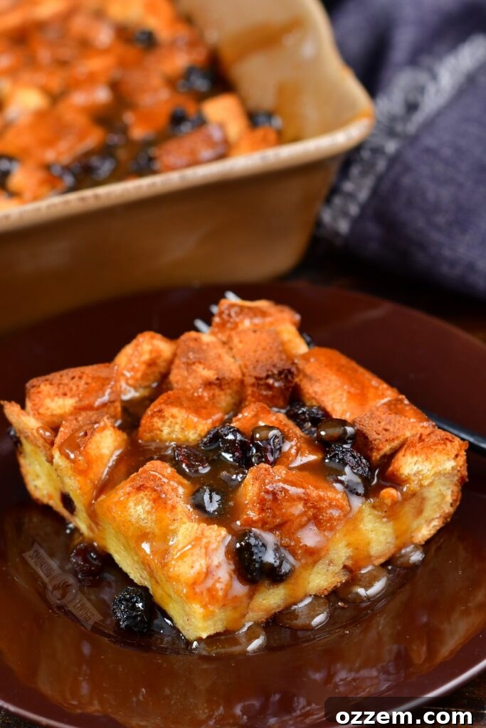 A single slice of smoked bourbon bread pudding served on a rustic brown plate, generously coated with the glistening brown sugar sauce.