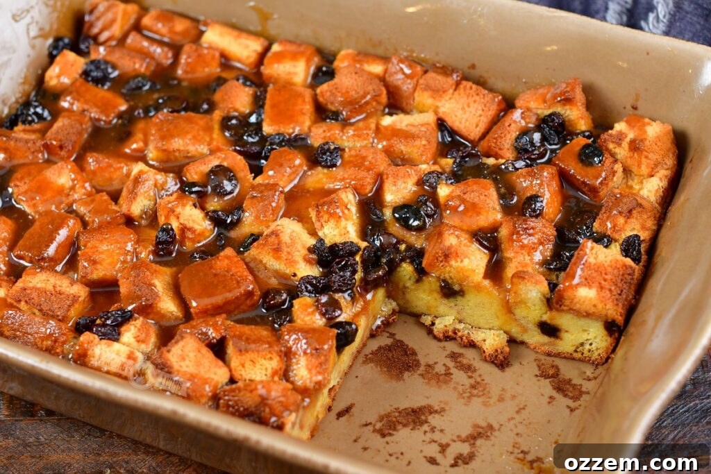 A beautiful smoked bread pudding in a baking dish with a slice neatly removed, revealing its moist, creamy interior filled with plump raisins.