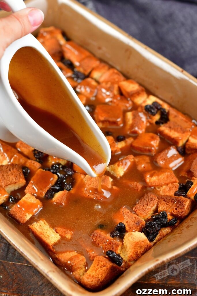 A stream of rich bourbon brown sugar sauce being poured generously over the top of a freshly baked smoked bread pudding in a baking dish.