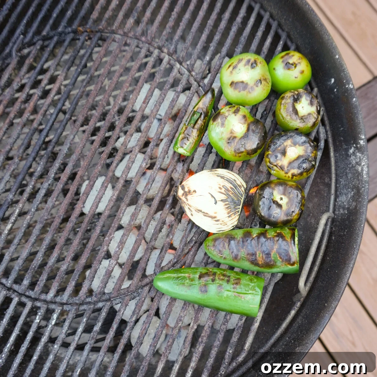 Assorted vegetables, including tomatillos, jalapeños, serrano peppers, and onions, being charred on a hot grill for the salsa verde.