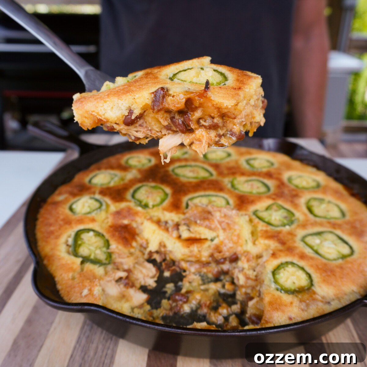 A perfectly portioned wedge of BBQ Chicken Cornbread Casserole being lifted from a rustic cast iron skillet, showcasing its golden-brown cornbread crust and savory, bubbling filling beneath.