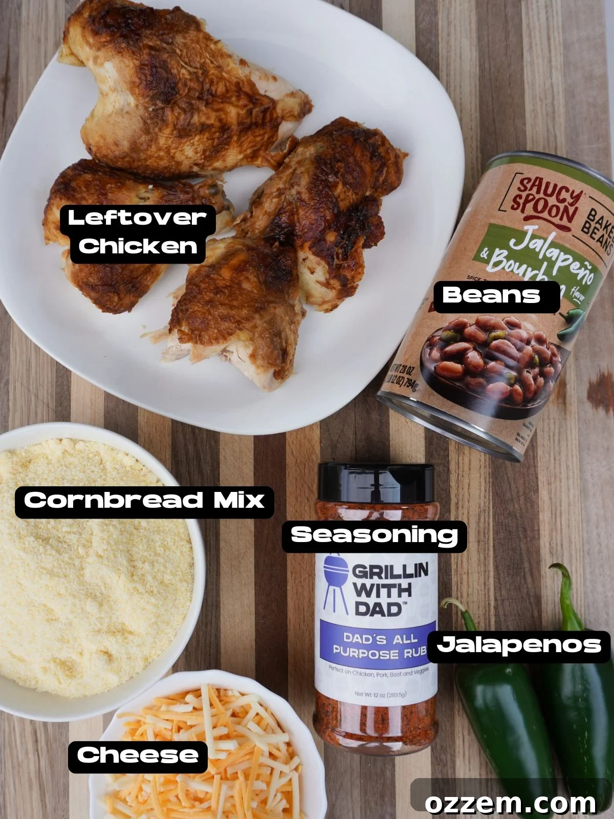 A beautifully arranged collection of fresh ingredients on a kitchen counter, featuring a bowl of savory shredded chicken, a full can of baked beans, a box of classic cornbread mix, a block of rich cheddar cheese, and vibrant fresh jalapeños, all poised for the casserole recipe.