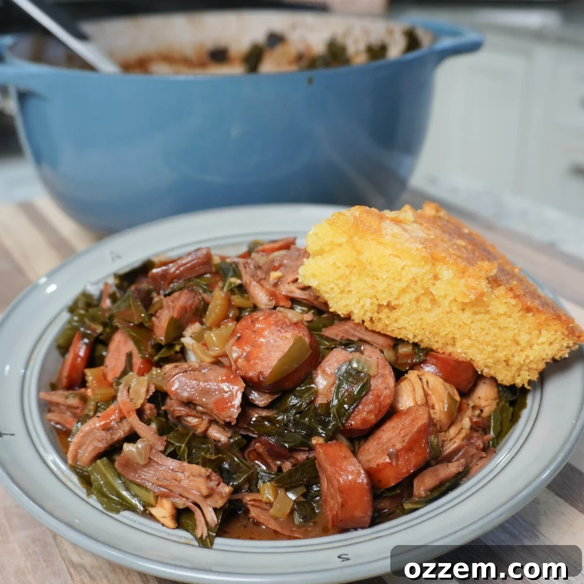 Collard Greens Cajun Gumbo plated with a cornbread wedge and blue pot in the background.