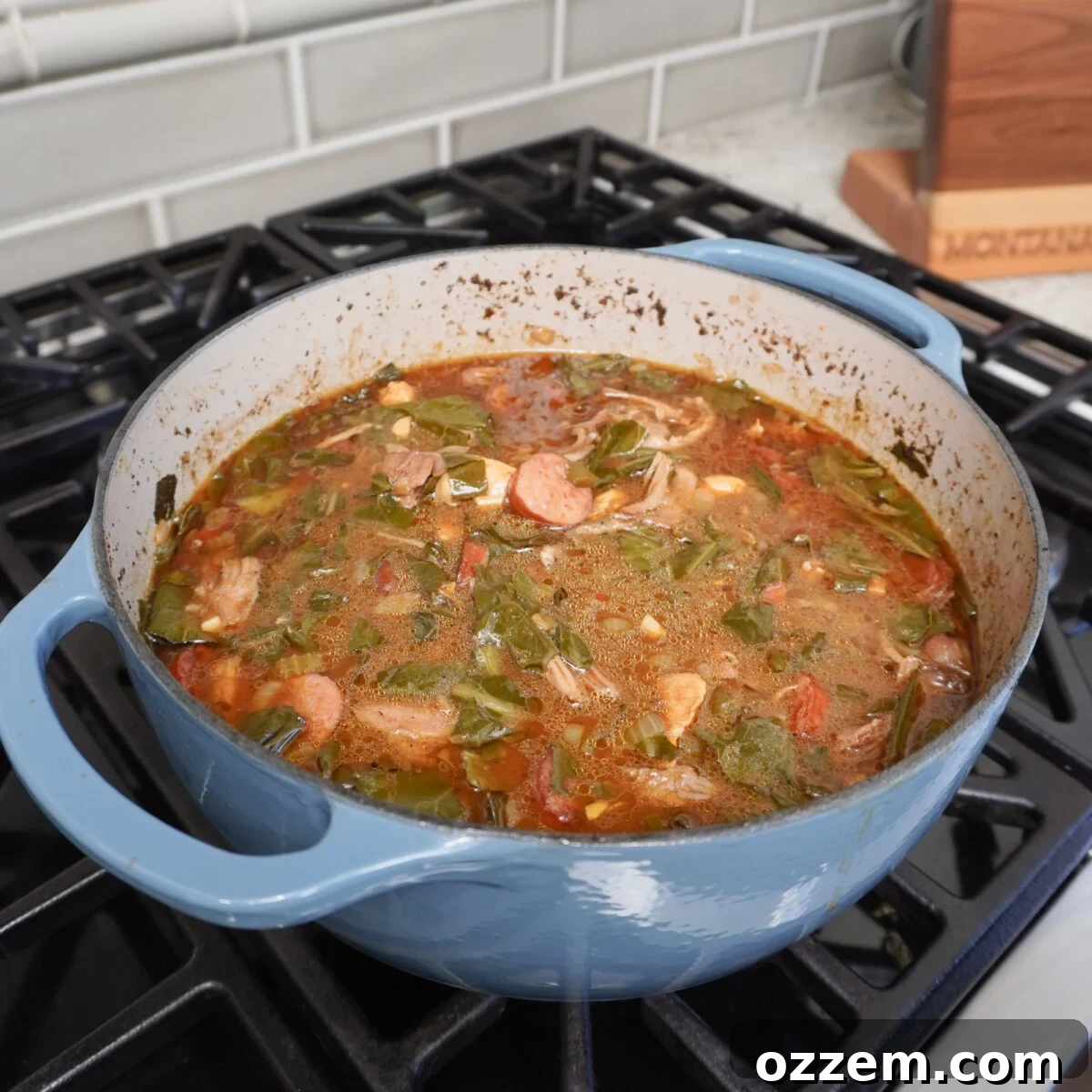 Collard greens simmering in a Dutch oven, submerged in the gumbo broth.
