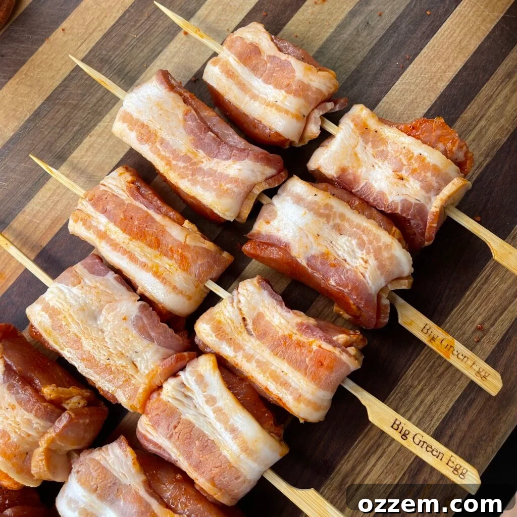 Savory Bacon Pork Skewers 3 Bacon-wrapped seasoned pork cubes on metal skewers, ready for the grill.