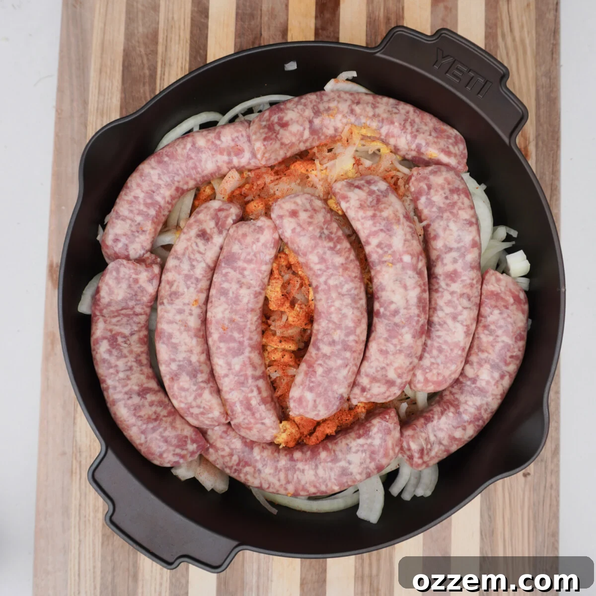 A large Dutch oven filled with sliced onions, chopped bacon, sauerkraut, and raw bratwurst, ready for the beer bath.