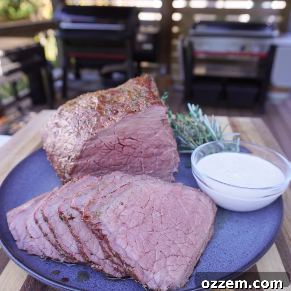 Smoked bottom round roast placed and sliced with a creamy garlic dipping sauce on the side.