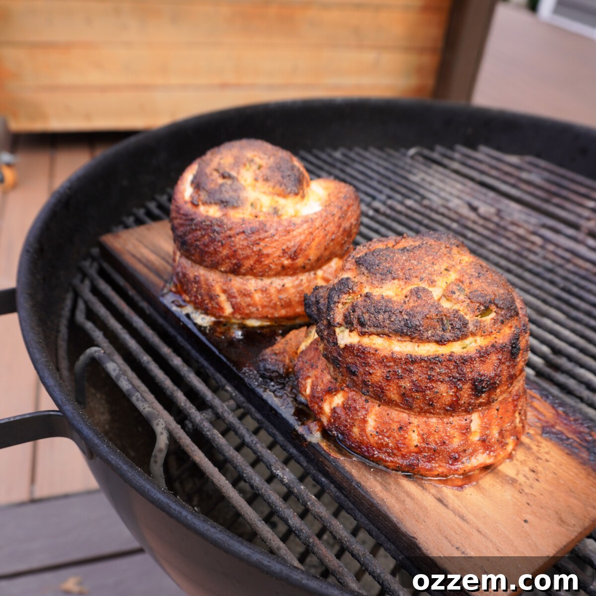 Grilled salmon pinwheels cooking on a cedar plank over a charcoal grill.